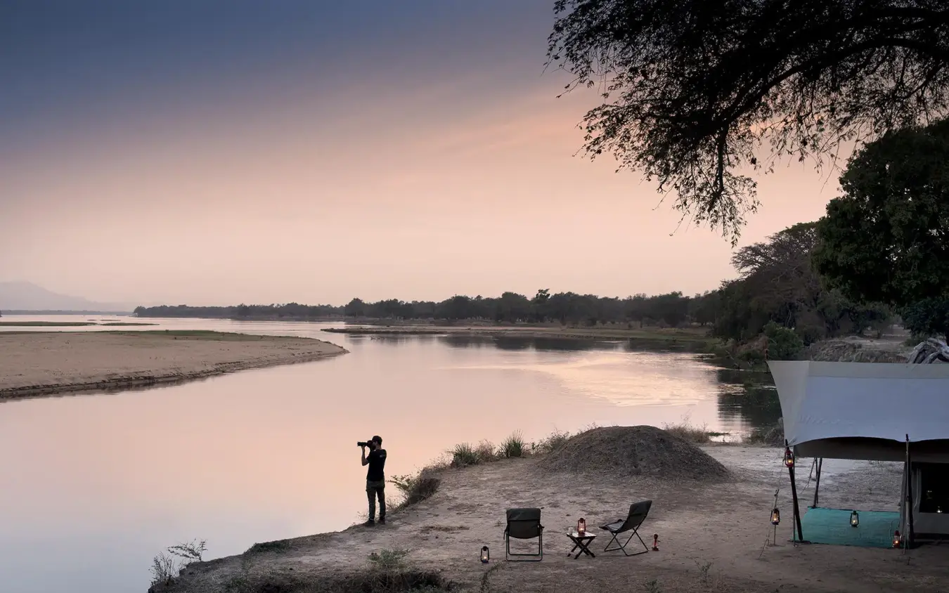 Safari camp overlooking river at sunset with guest viewing, Zambezi Expeditions, Mana Pools, Zimbabwe