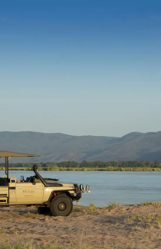 Safari vehicle parked on riverbank with mountain backdrop, Zambezi Expeditions, Mana Pools, Zimbabwe