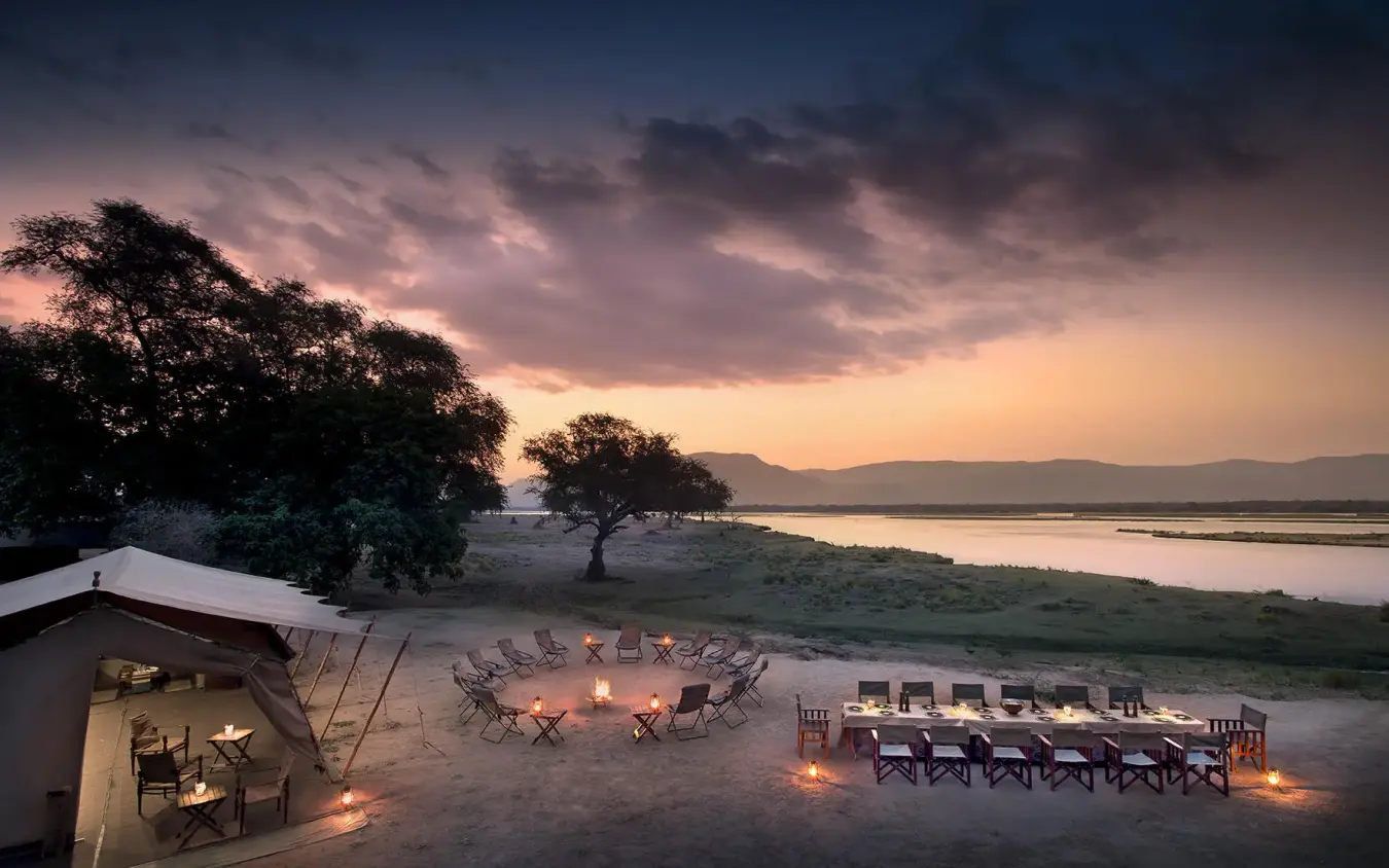 Riverside safari camp at dusk with illuminated seating areas, Zambezi Expeditions, Mana Pools, Zimbabwe