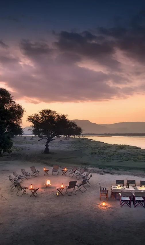 Riverside safari camp at dusk with illuminated seating areas, Zambezi Expeditions, Mana Pools, Zimbabwe