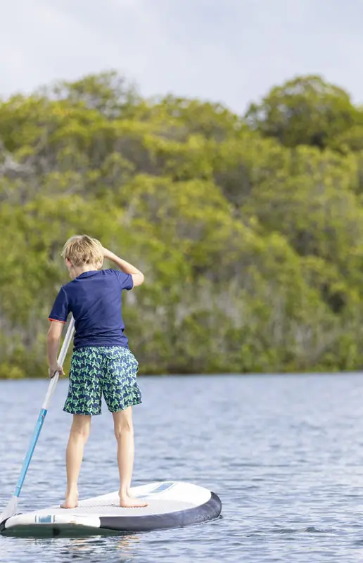Child stand-up paddleboarding on calm coastal water, Manda Bay, Lamu Archipelago, Kenya