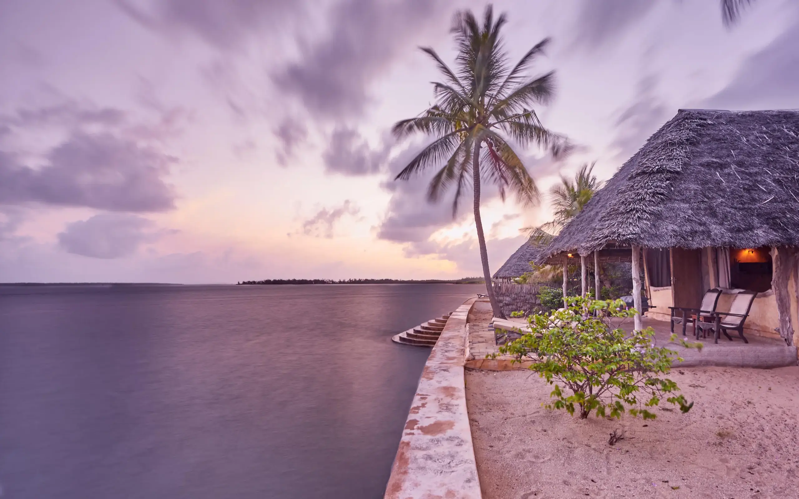 Beachfront bungalow at sunset with palm tree and ocean, Manda Bay, Lamu Archipelago, Kenya