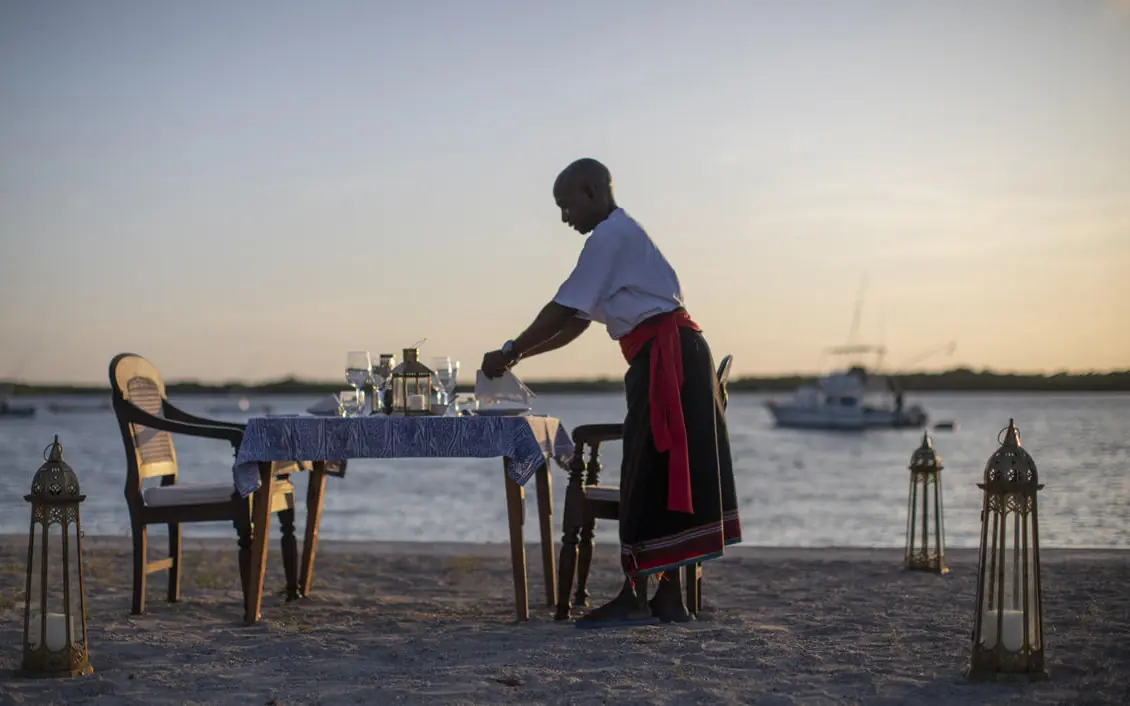 Staff member setting beachfront dinner table at sunset, Manda Bay, Lamu Archipelago, Kenya