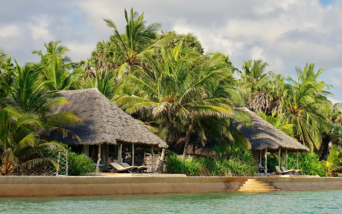 Thatched roof bungalows along waterfront with palm trees, Manda Bay, Lamu Archipelago, Kenya
