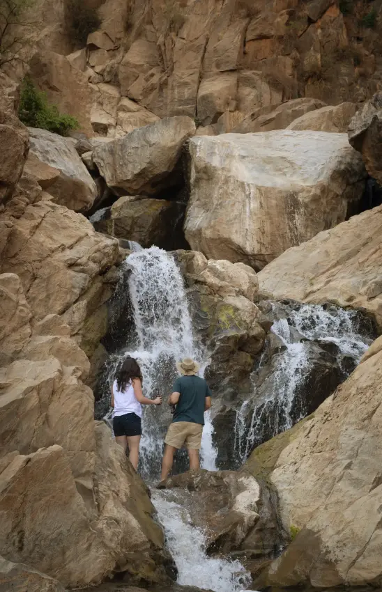 Hikers standing beneath cascading waterfall in rocky canyon, Manyara Green Camp, Lake Manyara, Tanzania