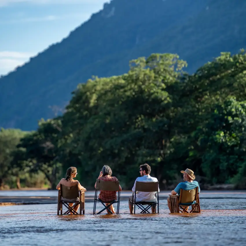 Four guests sitting in chairs in shallow river water, Manyara Green Camp, Lake Manyara, Tanzania