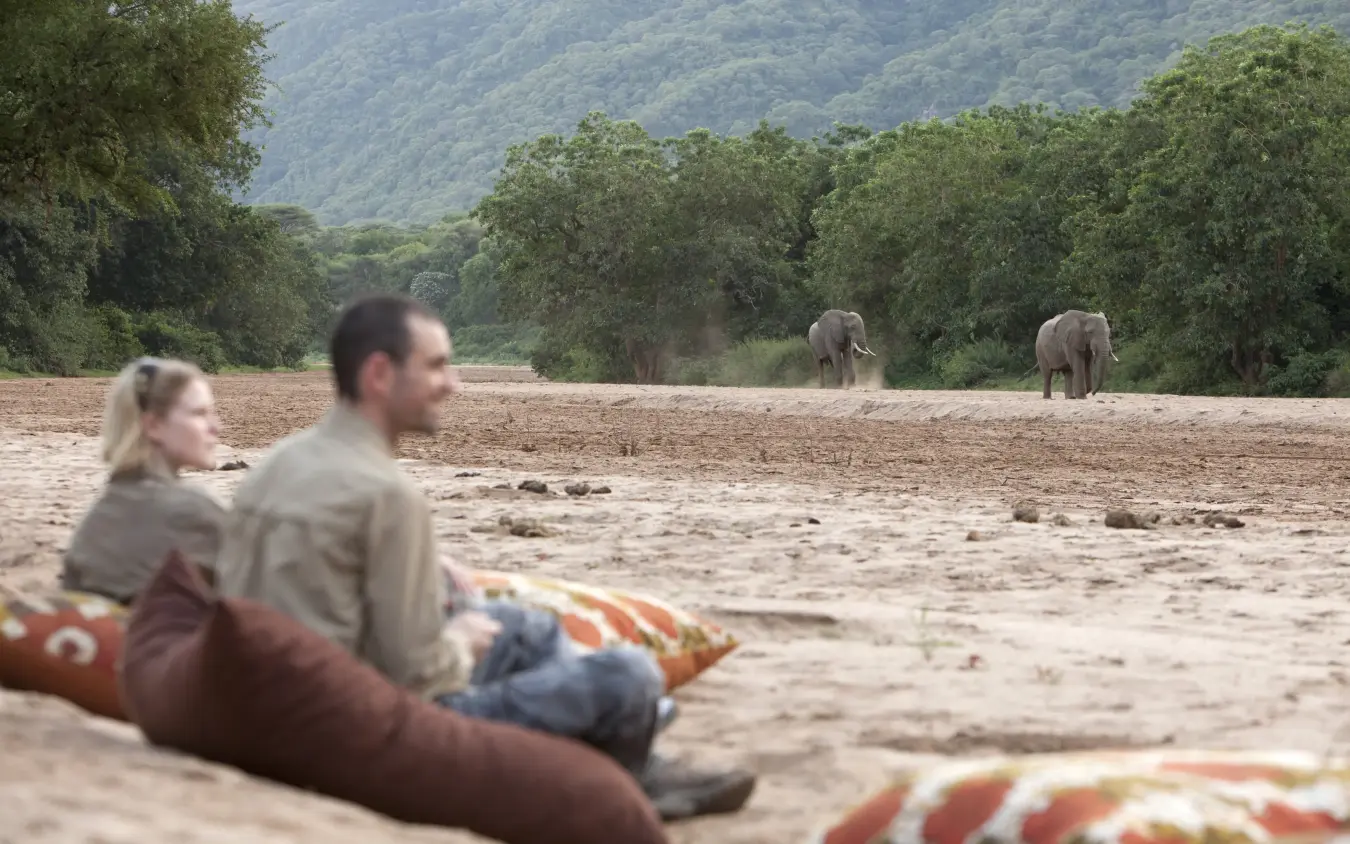 Guests relaxing on riverbed watching elephants in distance, Manyara Green Camp, Lake Manyara, Tanzania