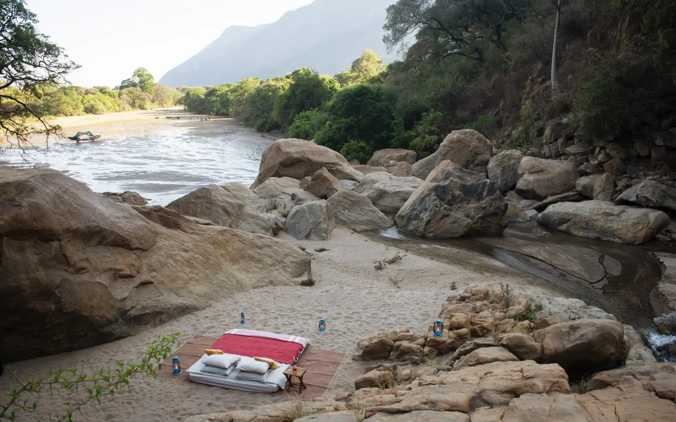 Riverside camping setup with boulders and mountain backdrop, Manyara Green Camp, Lake Manyara, Tanzania