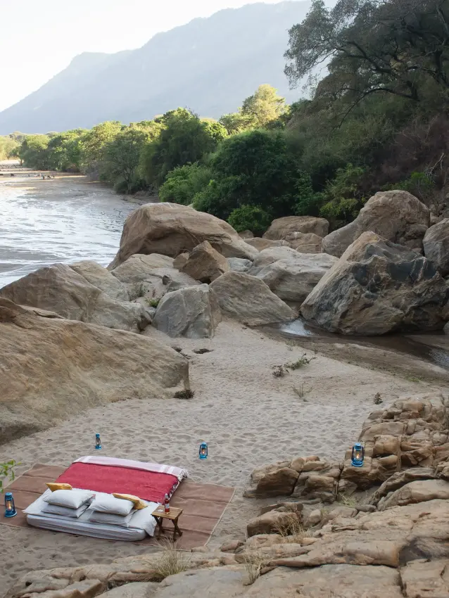 Riverside camping setup with boulders and mountain backdrop, Manyara Green Camp, Lake Manyara, Tanzania