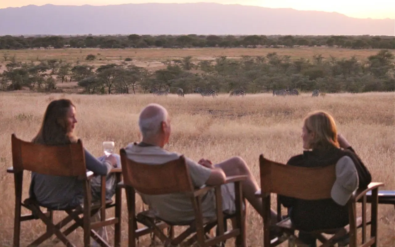 Three guests in safari chairs viewing wildlife at sunset with savanna landscape, Manyara Ranch, Lake Manyara, Tanzania