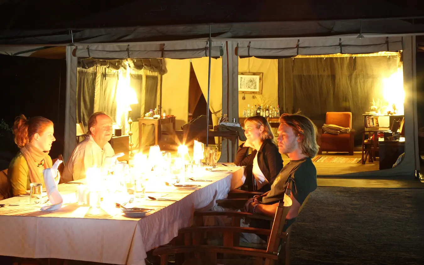 Guests dining outdoors at candlelit table beside lit lodge at night, Manyara Ranch, Lake Manyara, Tanzania