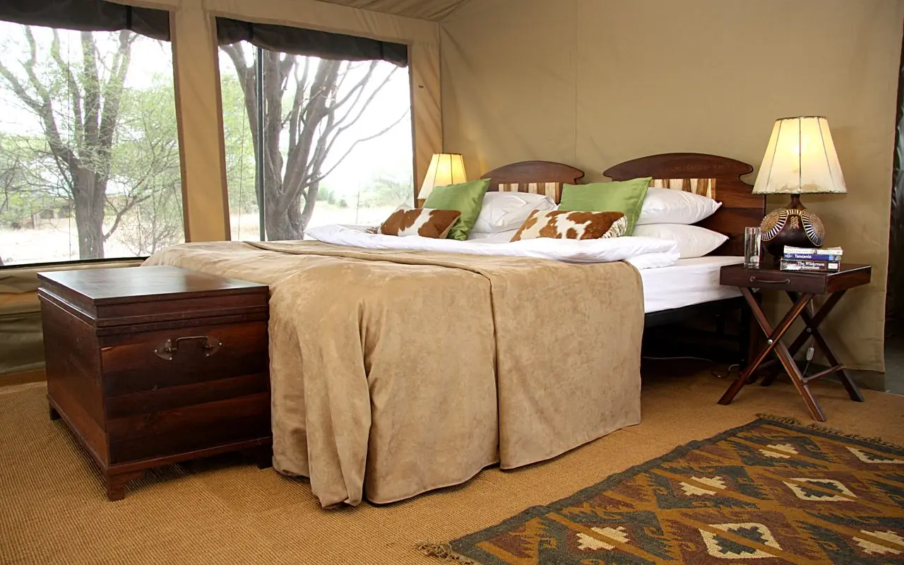 Luxury bedroom with wooden furniture overlooking natural landscape through large windows, Manyara Ranch, Lake Manyara, Tanzania