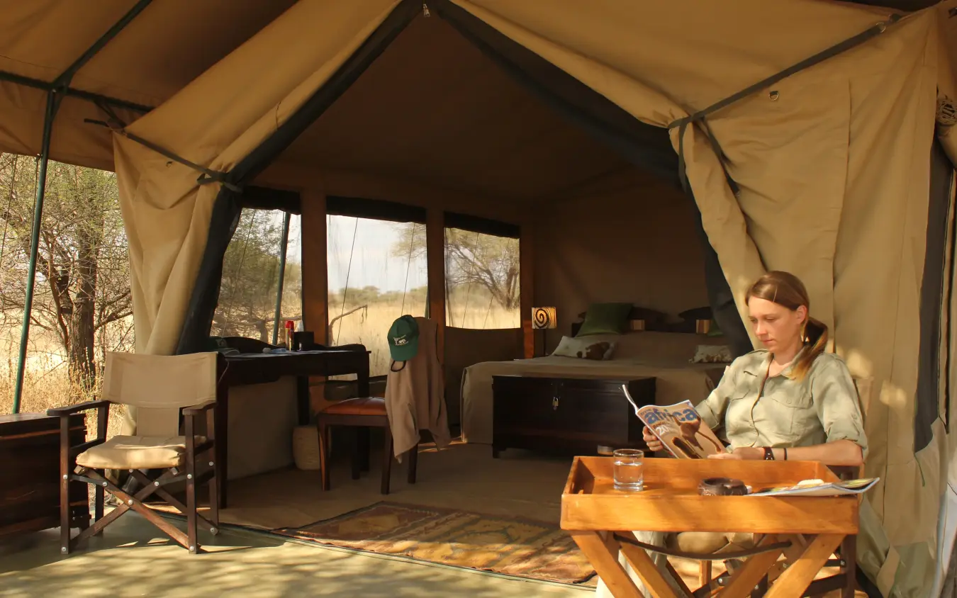 Woman reading inside safari tent with large windows overlooking savanna, Manyara Ranch, Lake Manyara, Tanzania