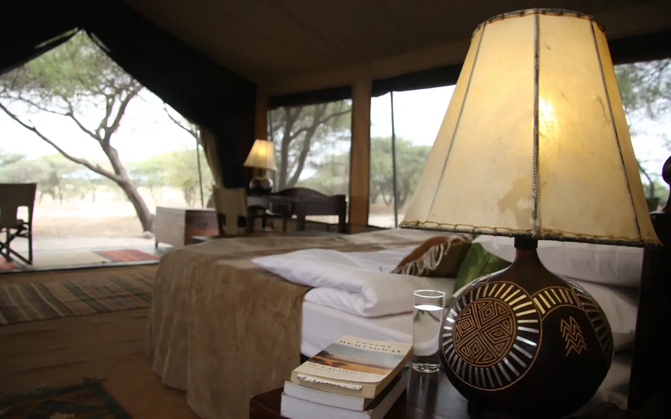 Luxury safari tent interior with bed, lamp and savanna view through open canvas, Manyara Ranch, Lake Manyara, Tanzania
