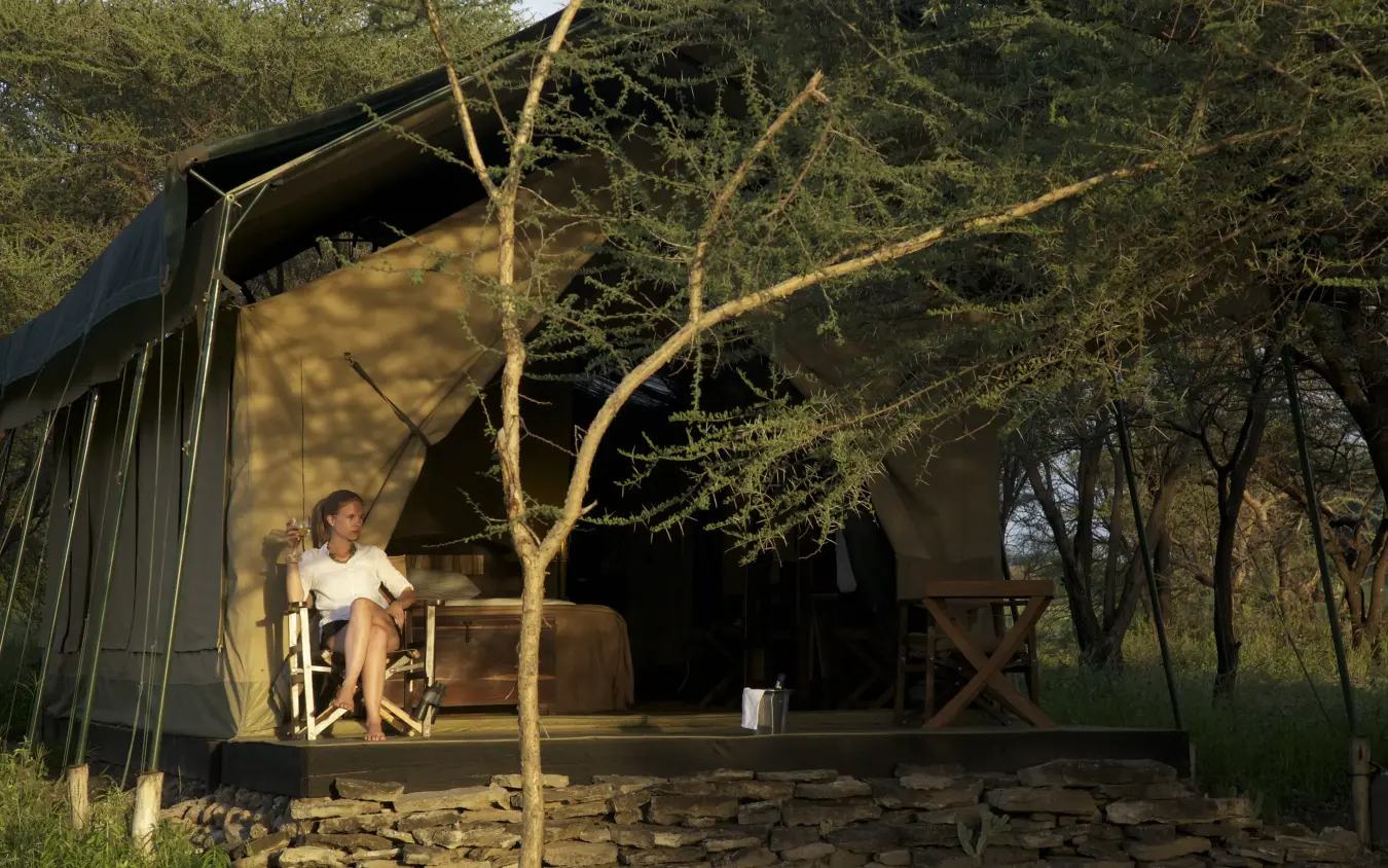 Guest relaxing on safari lodge deck at dusk with lantern lighting, Manyara Ranch, Lake Manyara, Tanzania