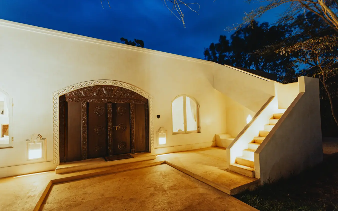 Illuminated white building exterior with wooden door and stairs, Manzili House, Nairobi, Kenya