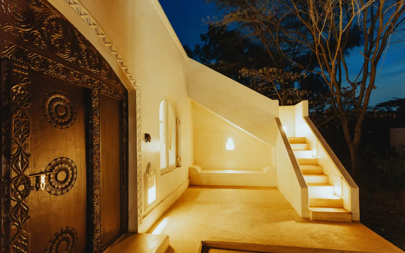 Illuminated modern lodge entrance with carved wooden doors at dusk, Manzili House, Nairobi, Kenya