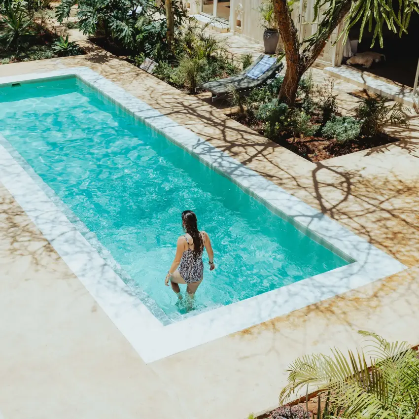 Woman wading in turquoise swimming pool surrounded by trees, Manzili House, Nairobi, Kenya