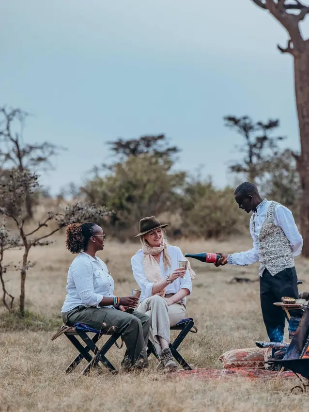 Guests enjoying wine service around campfire in savanna, Mara Nyika Camp, Maasai Mara, Kenya