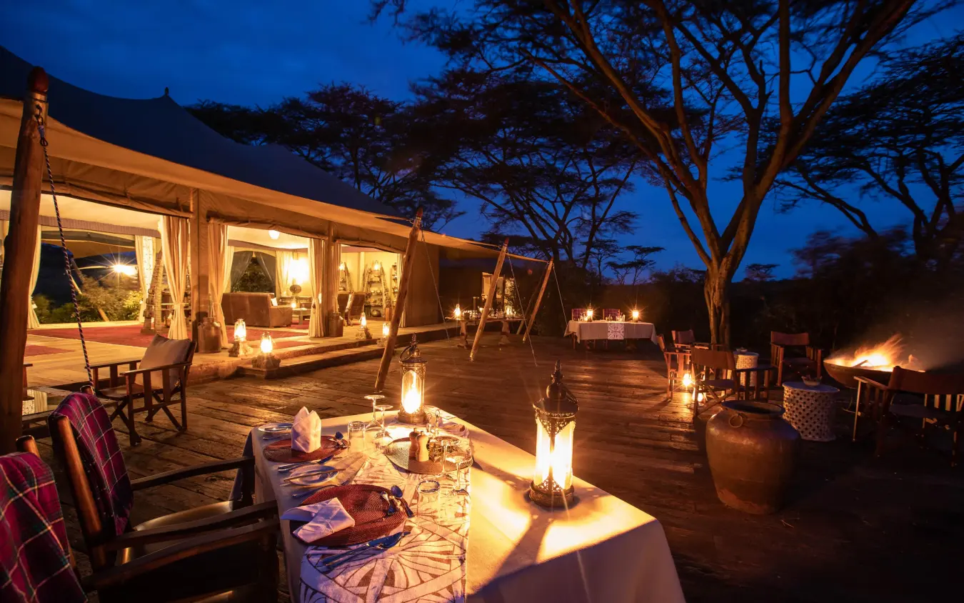 Outdoor dining deck at night with lanterns and acacia trees, Mara Nyika Camp, Maasai Mara, Kenya