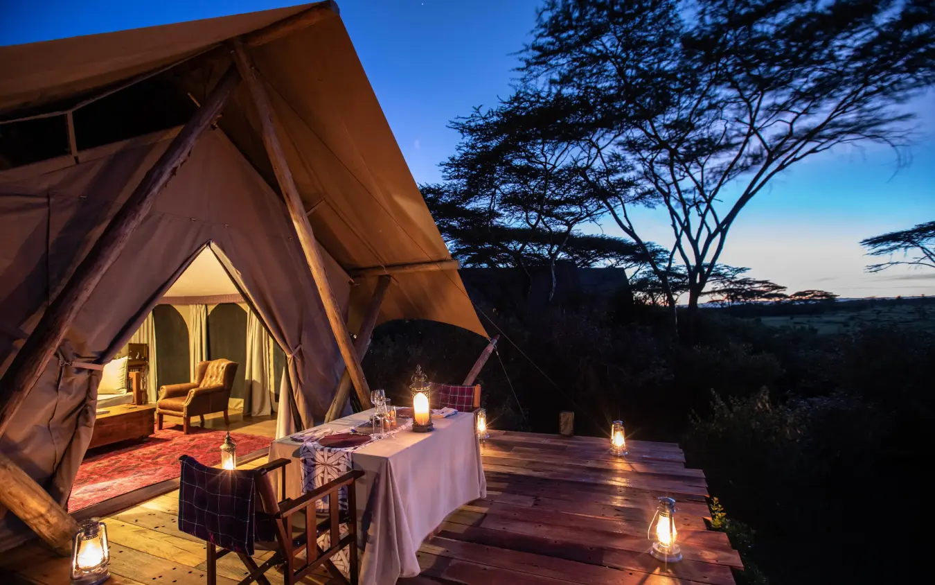 Illuminated safari tent with dining setup at dusk, Mara Nyika Camp, Maasai Mara, Kenya