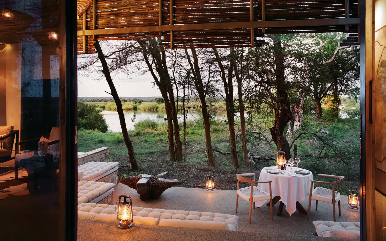 Riverside deck with dining setup overlooking trees and water, Matetsi River Lodge, Victoria Falls, Zimbabwe