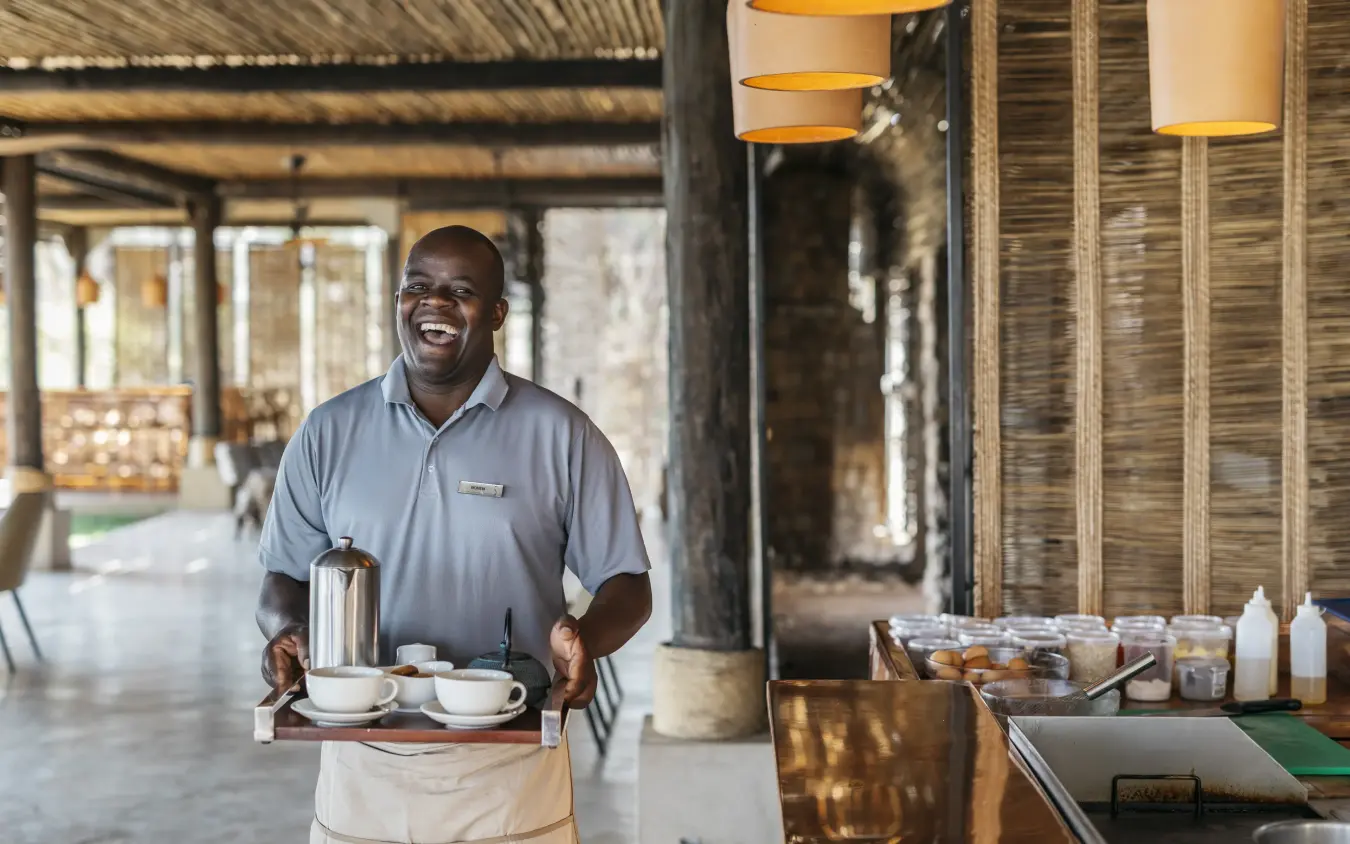 Staff member serving coffee in lodge interior space, Matetsi River Lodge, Victoria Falls, Zimbabwe