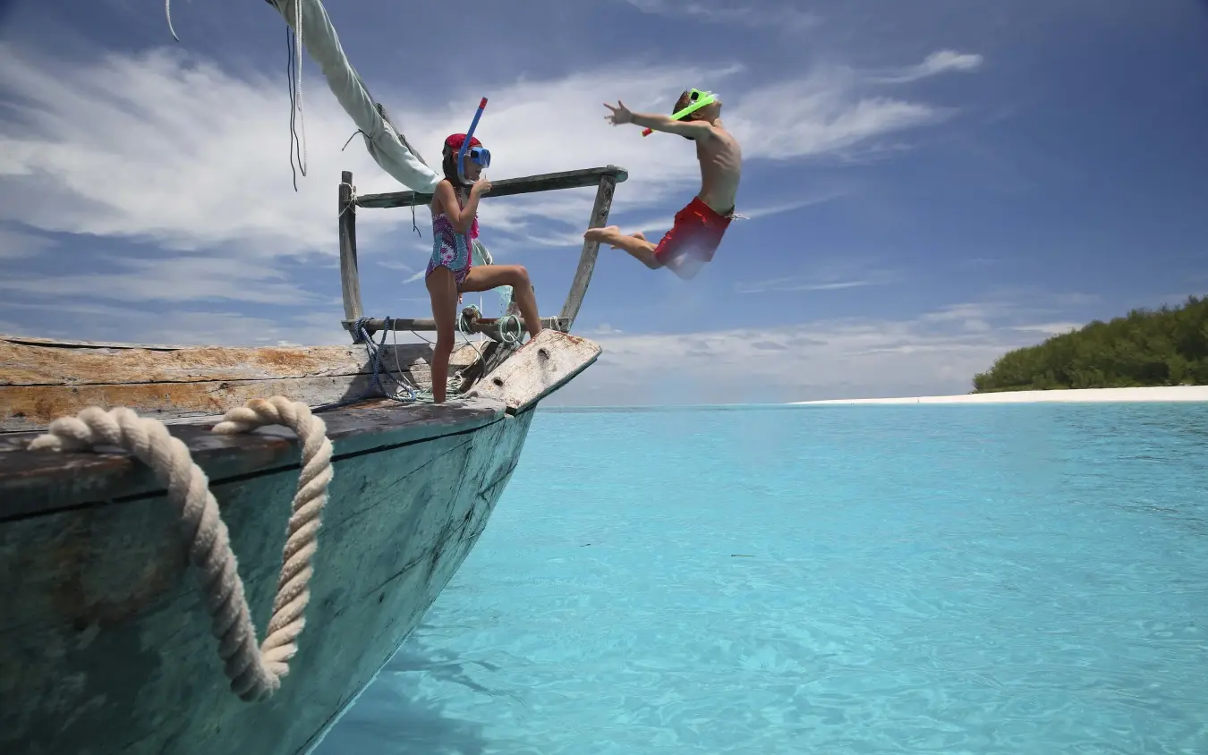 Guests jumping from traditional wooden boat into turquoise water, Mnemba Island, Zanzibar & Pemba, Tanzania