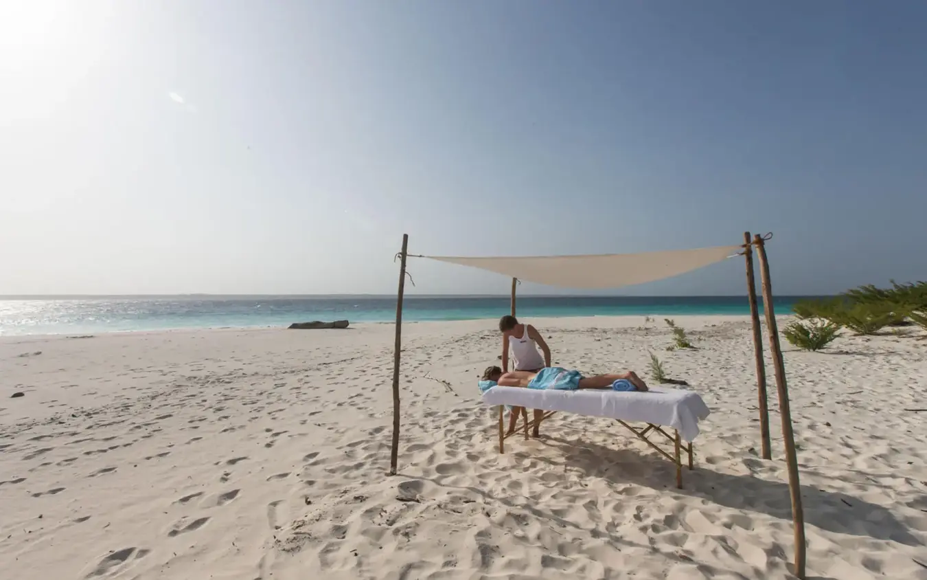 Guest relaxing under beach canopy with turquoise ocean, Mnemba Island, Zanzibar & Pemba, Tanzania
