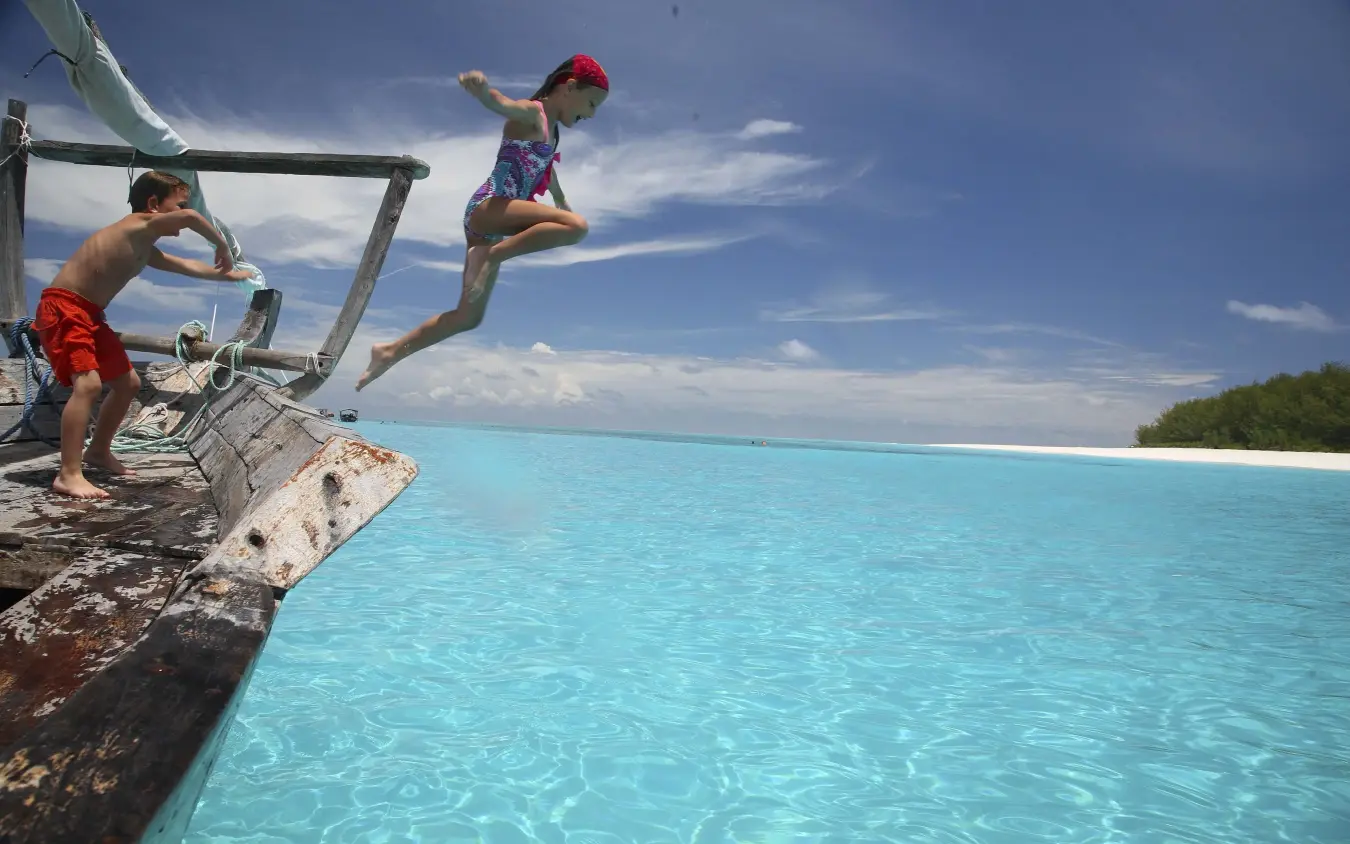 Children jumping from wooden boat into turquoise ocean water, Mnemba Island, Zanzibar & Pemba, Tanzania
