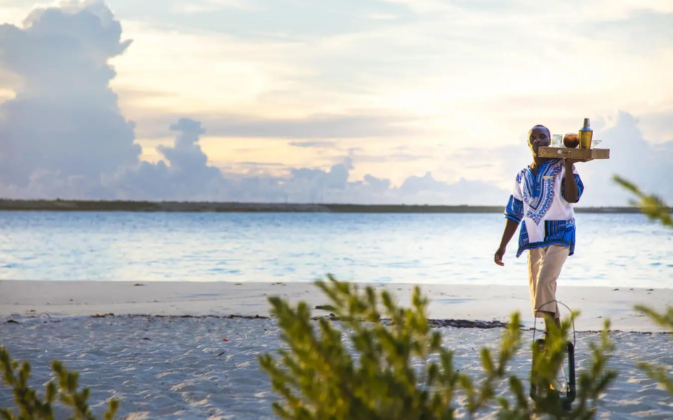 Guest carrying telescope walking on beach at sunset, Mnemba Island, Zanzibar & Pemba, Tanzania