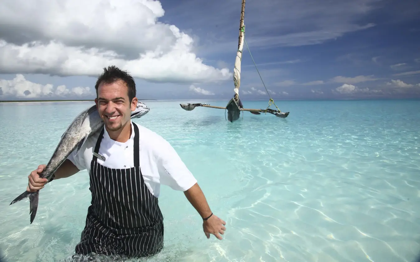 Chef holding fresh caught fish in shallow tropical waters, Mnemba Island, Zanzibar & Pemba, Tanzania