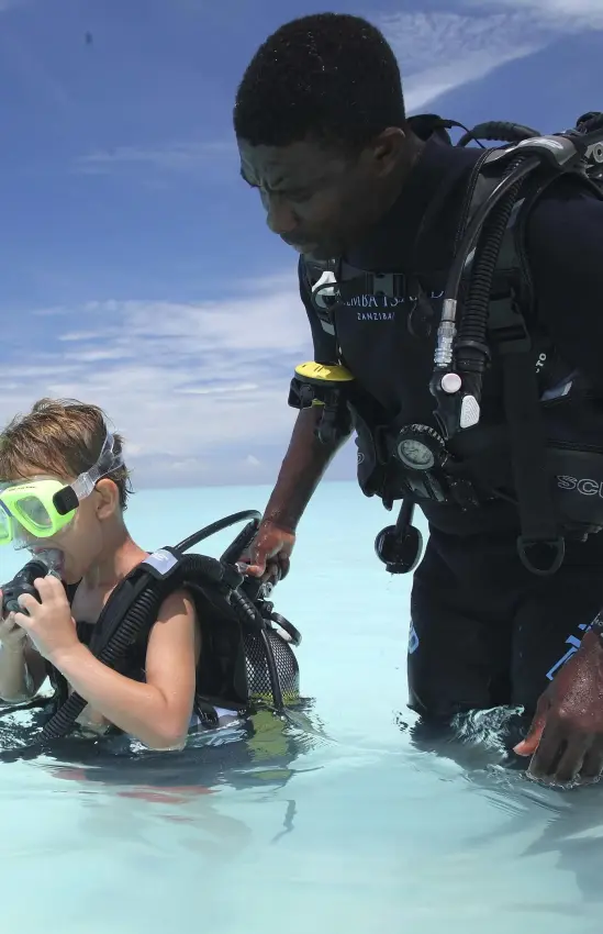 Scuba diving instructor helping young guest in shallow water, Mnemba Island, Zanzibar & Pemba, Tanzania