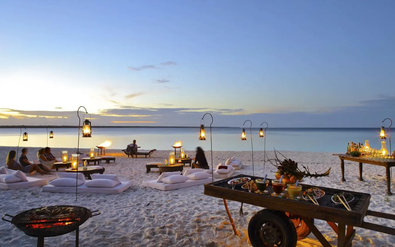 Beach dining setup at sunset with lanterns and fire pits, Mnemba Island, Zanzibar & Pemba, Tanzania