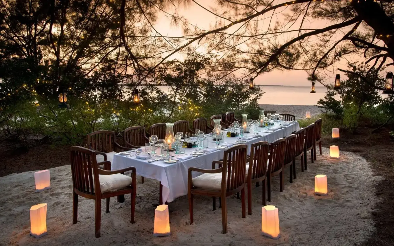 Beachfront dinner table set under trees at dusk, Mnemba Island, Zanzibar & Pemba, Tanzania