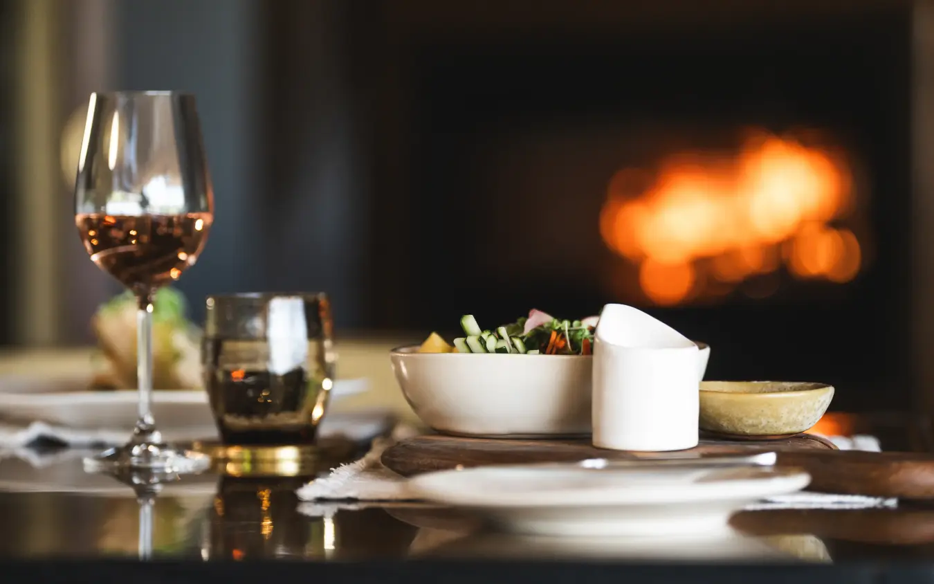 Fireplace dining setup with wine glass and plated food in evening light, Mombo Camp, The Okavango Delta, Botswana