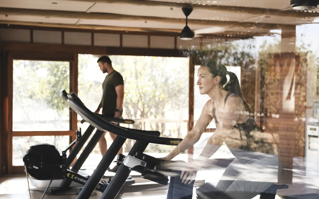 Fitness center with guests exercising on treadmills overlooking natural landscape, Mombo Camp, The Okavango Delta, Botswana