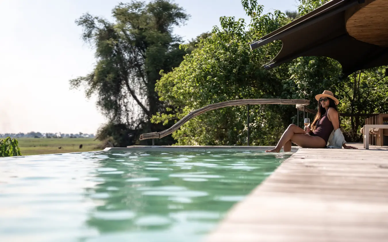 Woman relaxing by infinity pool overlooking floodplain landscape, Mombo Camp, The Okavango Delta, Botswana