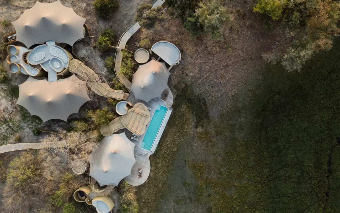 Aerial view of luxury lodge with pool and thatched structures surrounded by woodland, Mombo Camp, The Okavango Delta, Botswana