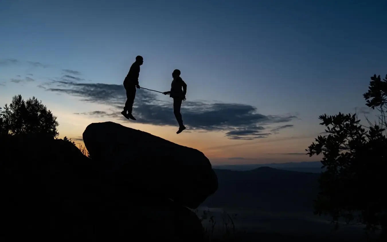 Two people silhouetted on large boulder at dusk with valley landscape below, Moon’s Camp, Laikipia Highlands, Kenya