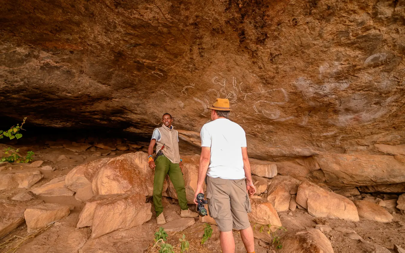 Two hikers exploring rock shelter with ancient cave paintings, Moon’s Camp, Laikipia Highlands, Kenya