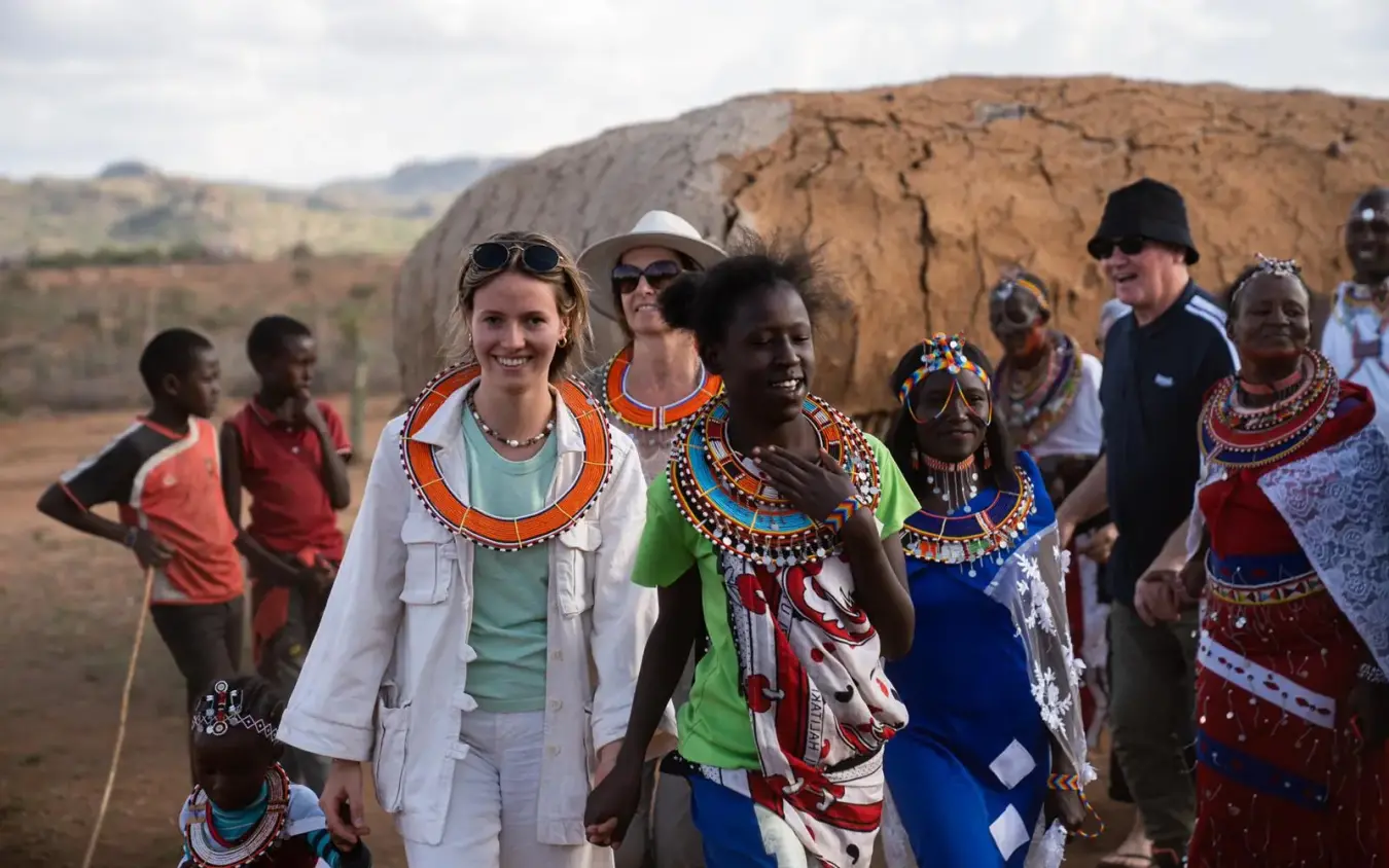 Tourists wearing beaded necklaces with local community members near traditional dwelling, Moon’s Camp, Laikipia Highlands, Kenya