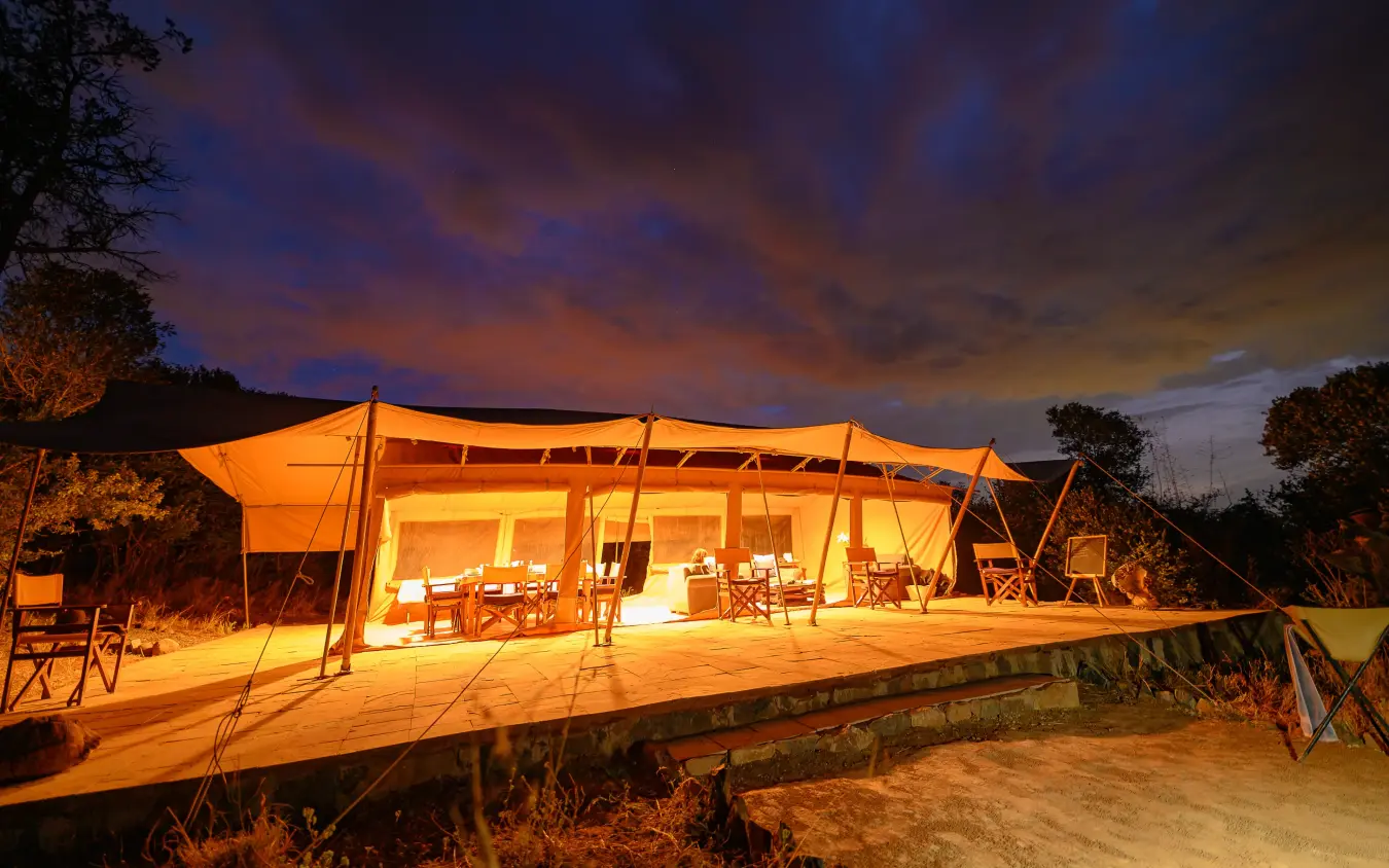 Illuminated safari tent with dining area at dusk under dramatic sky, Moon’s Camp, Laikipia Highlands, Kenya