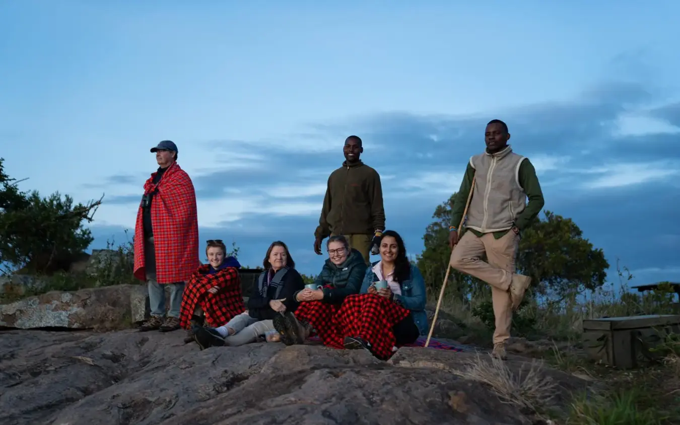 Group of guests gathered on rocky outcrop at dusk with savanna landscape, Moon’s Camp, Laikipia Highlands, Kenya