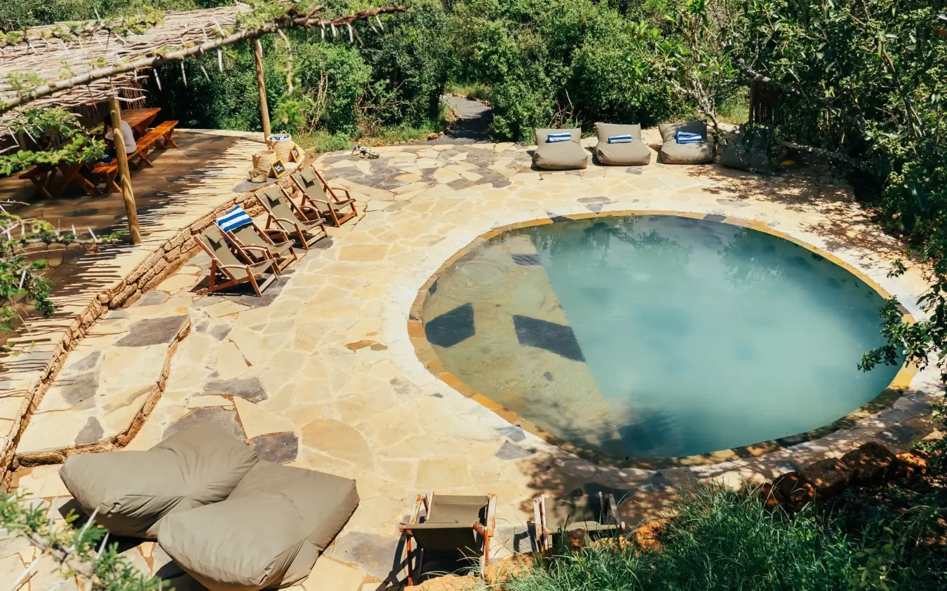 Natural hot spring pool with loungers in bush setting surrounded by vegetation, Moon’s Camp, Laikipia Highlands, Kenya