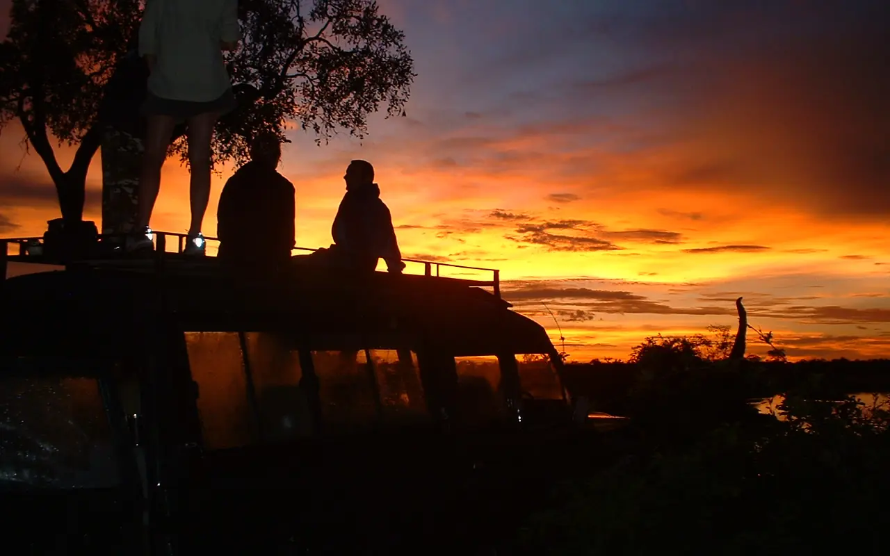 Guests silhouetted on wooden deck at sunset over water