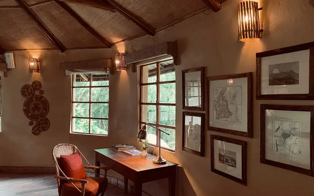 Interior office space with desk, wooden beams, and framed artwork, Mount Gahinga Lodge, Mgahinga National Park, Uganda