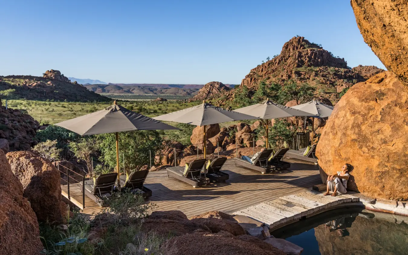 Luxury deck with loungers and shade umbrellas among granite boulders overlooking valley, Mowani Mountain Camp, Damaraland, Namibia