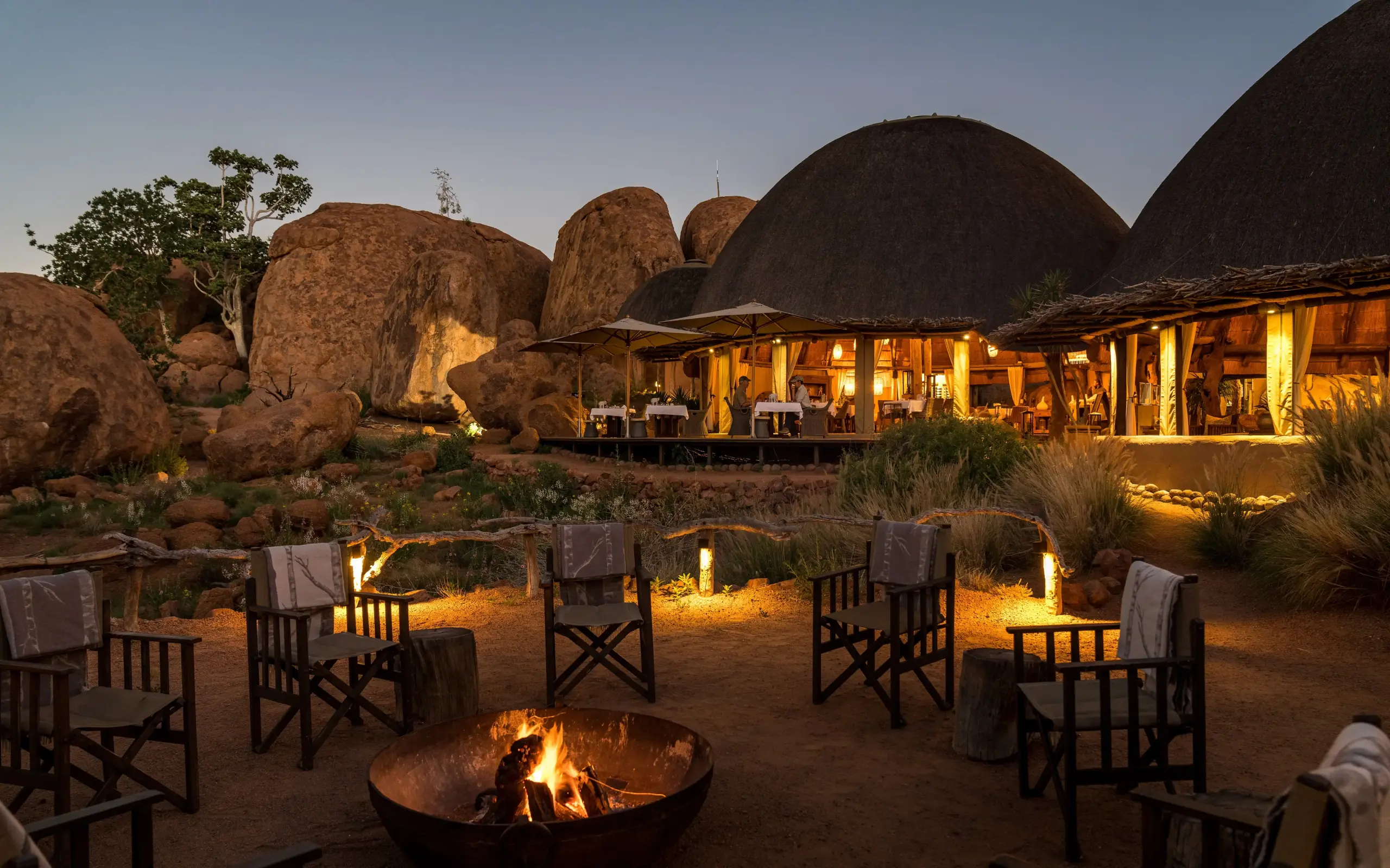 Evening campfire with dome-shaped thatched structures and boulder formations, Mowani Mountain Camp, Damaraland, Namibia