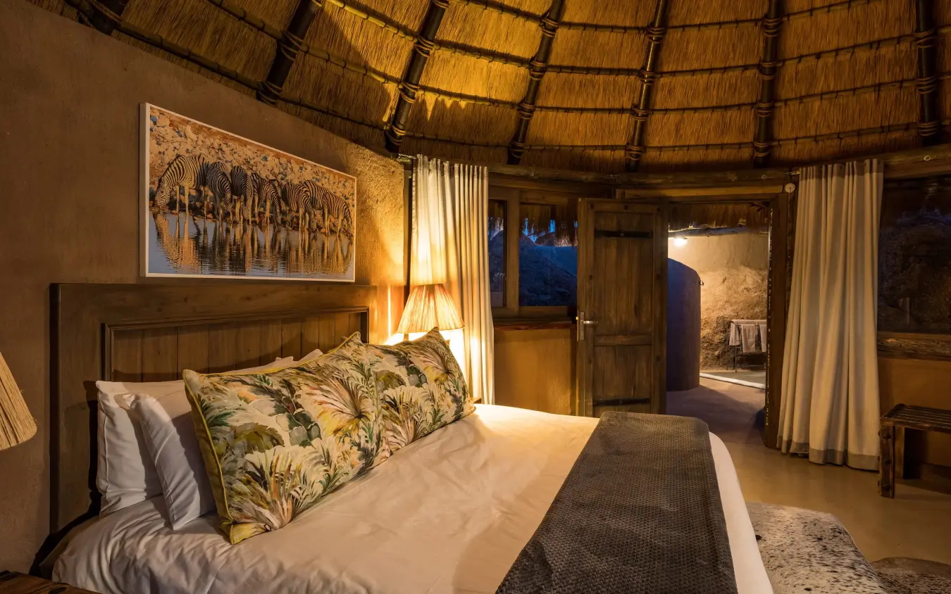Luxury safari lodge bedroom with thatched roof and savanna views at dusk, Mowani Mountain Camp, Damaraland, Namibia